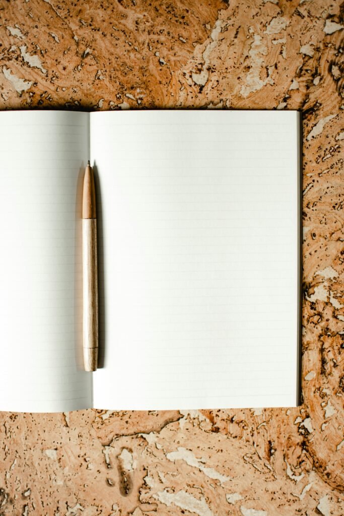 pexels photo 8059663 8059663 Open notebook with wooden pen on a cork-textured surface, ideal for stationery mockups.